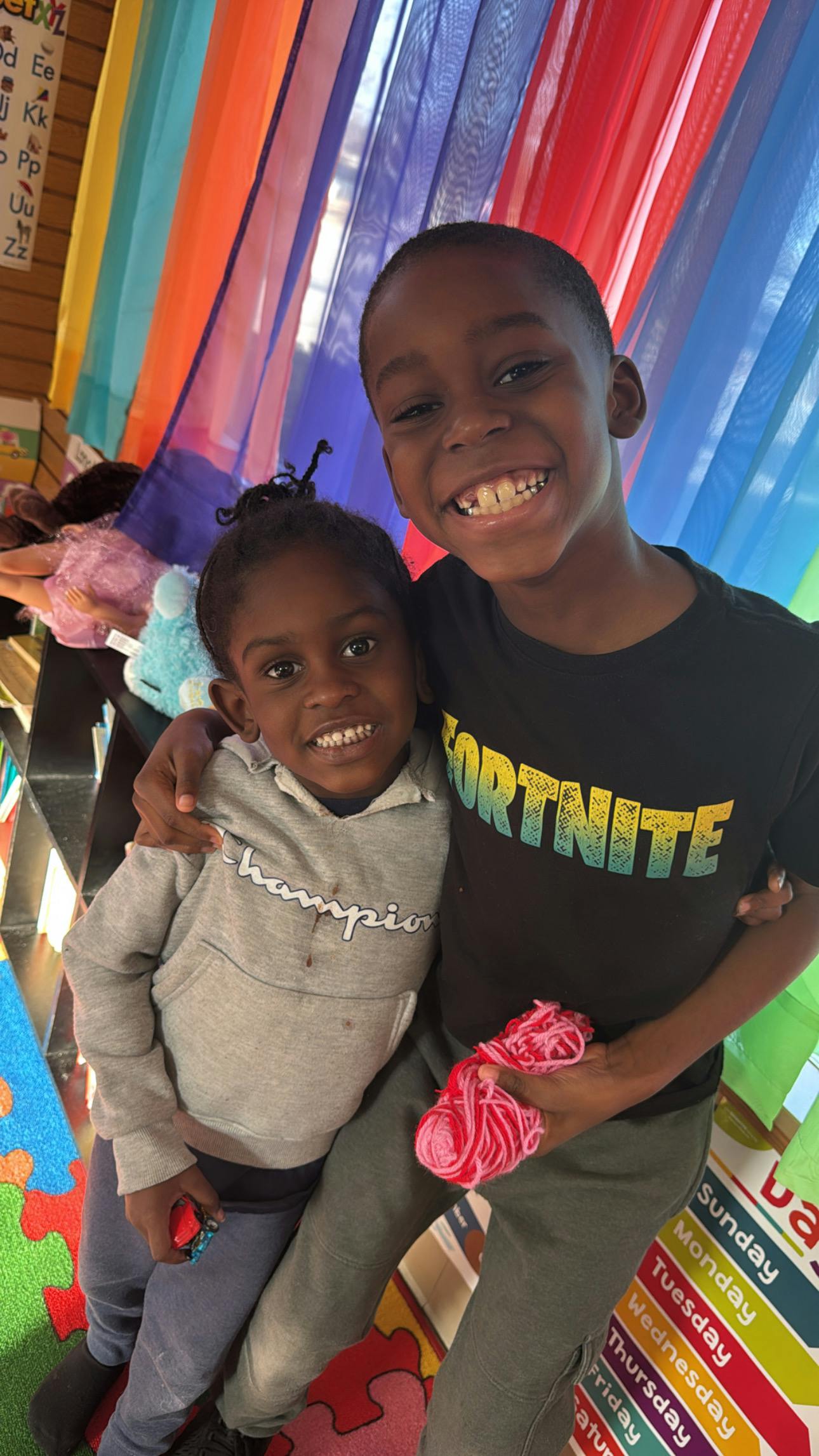 Two children smiling, one wearing a black shirt with 'FORTNITE' text