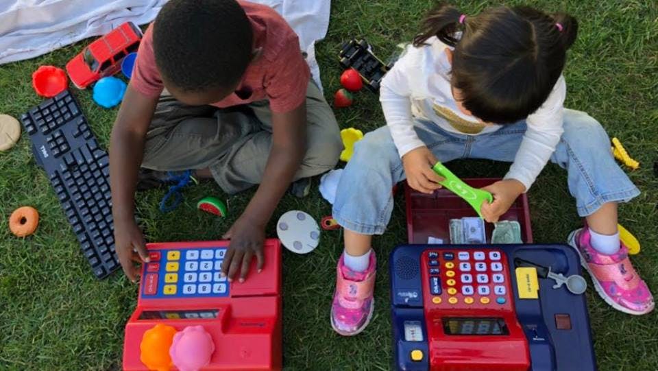 Two children playing with toy cash registers on grass