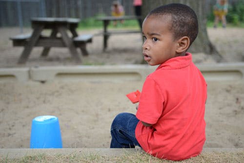 Child sitting in a sandbox with a blue bucket