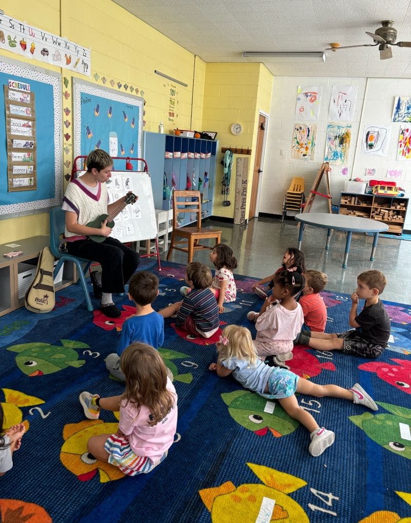 Person playing ukulele for children in a classroom