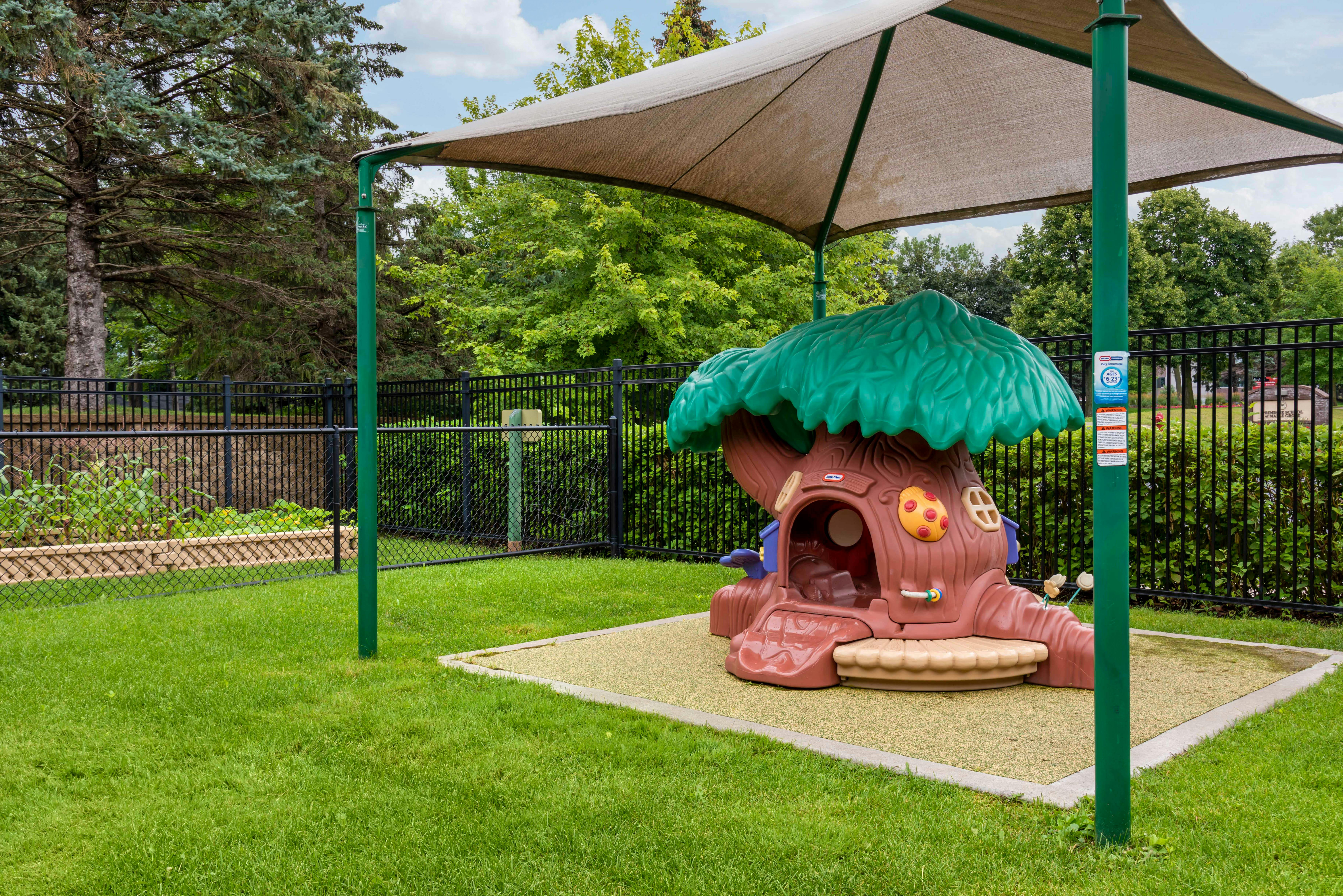 children's play structure shaped like a tree under a shade canopy