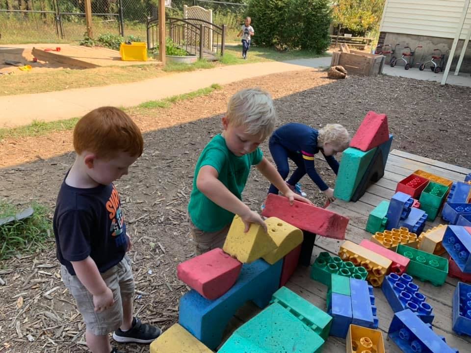 Three children playing with colorful building blocks outdoors