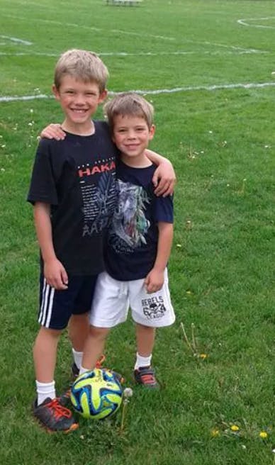Two children standing on a grassy field with a soccer ball