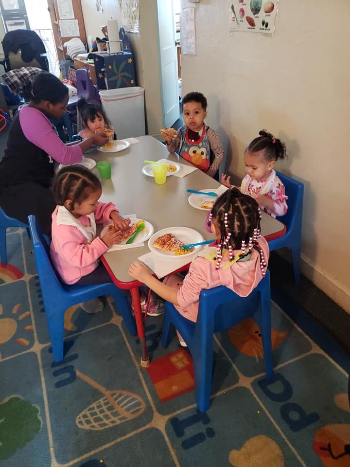 Adult and four children eating at a table in a classroom
