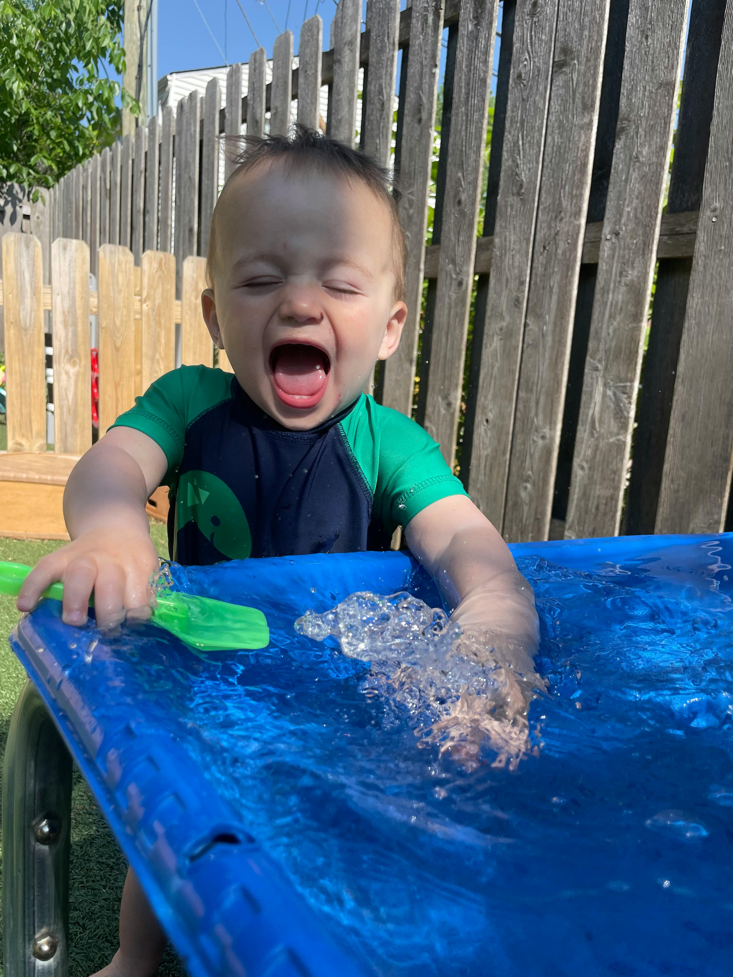 Child playing in water with a green toy