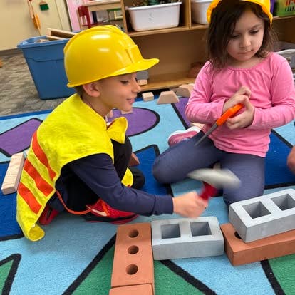 Two children in hard hats playing with toy bricks and tools