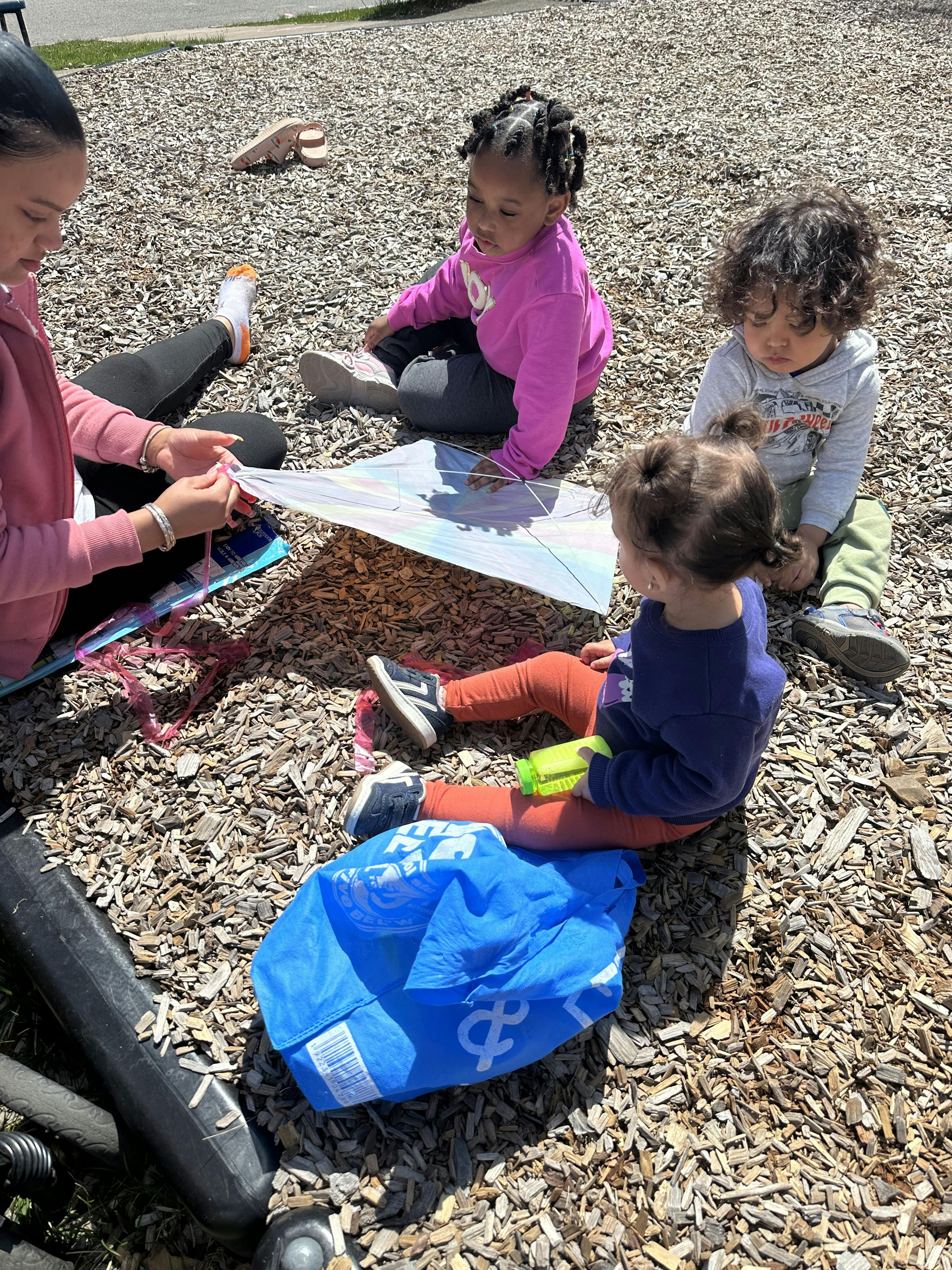 Adult and three children sitting on wood chips assembling a kite