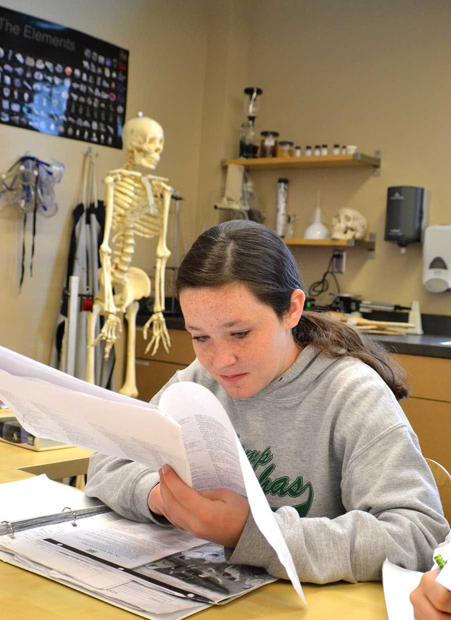 Teen reading papers in a classroom with a skeleton model