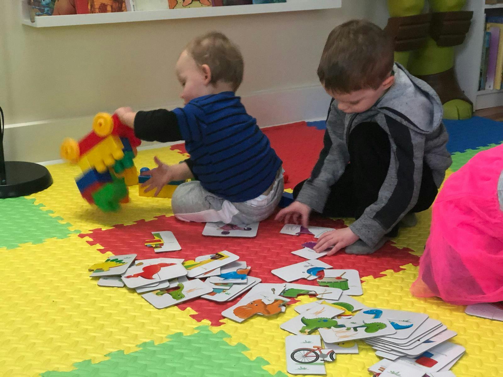 Two children playing with toys and cards on a colorful mat