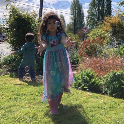 Child reaching for bubbles outdoors, another child in background