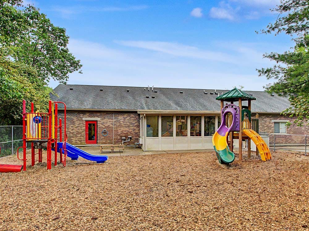 Playground with two slides on wood chips in front of a brick building