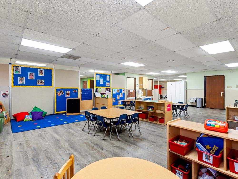 An empty children's classroom with small tables and chairs, and a play area