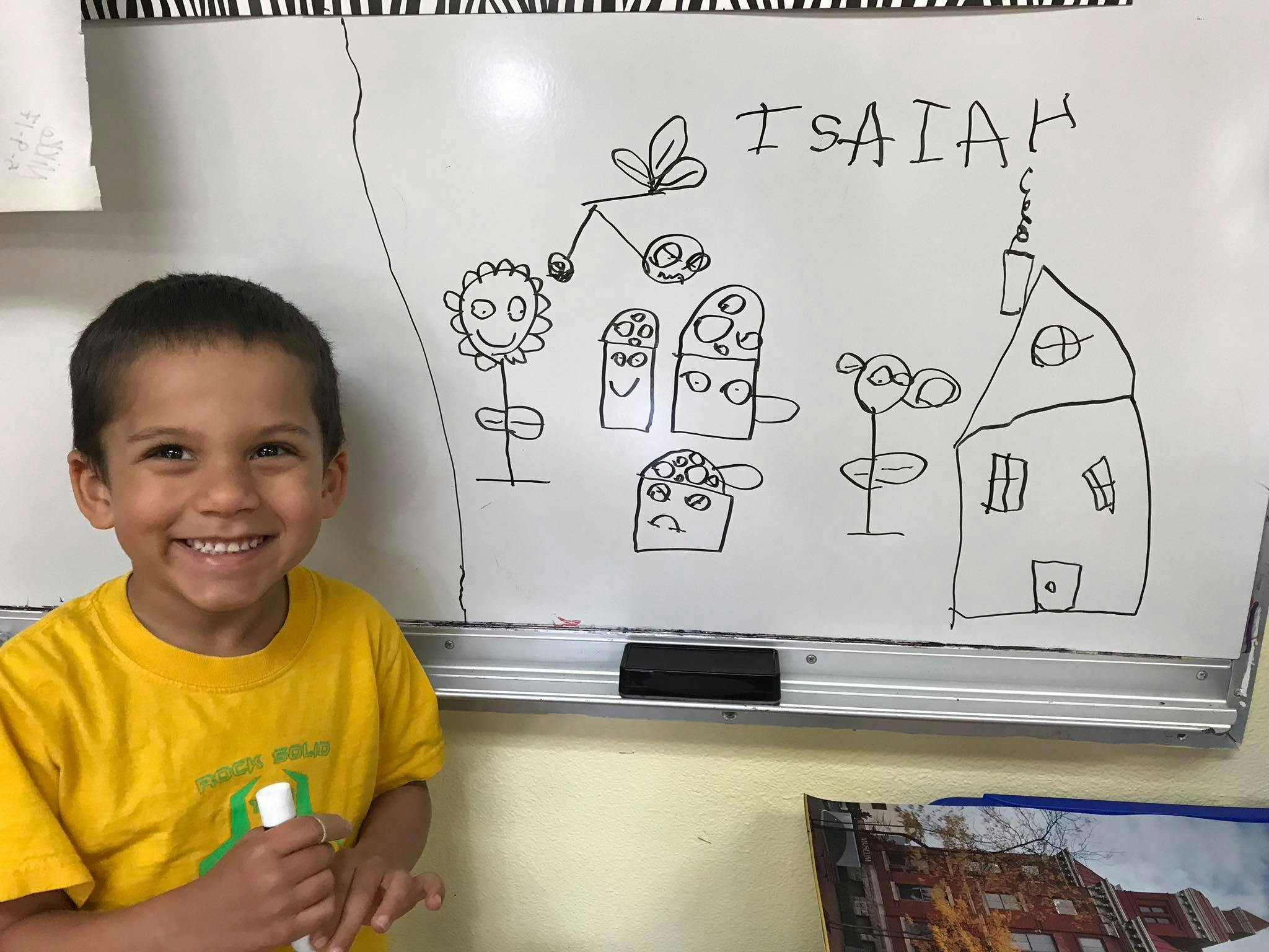 Child in yellow shirt standing next to a whiteboard with drawings