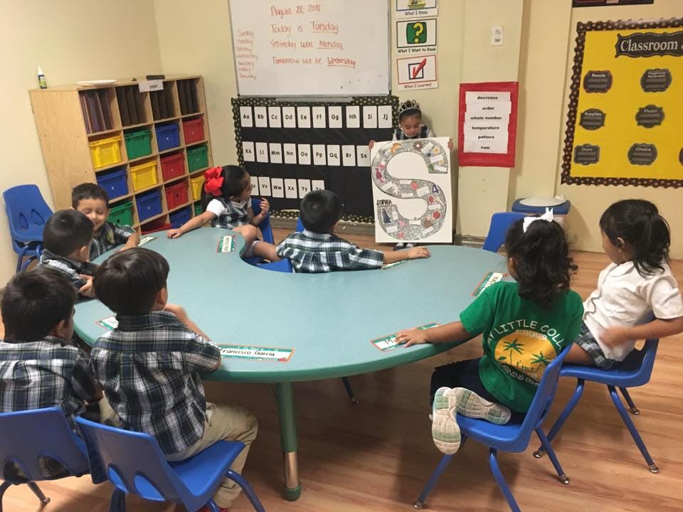 Children sitting around a table in a classroom, one child holding up a sign with an S