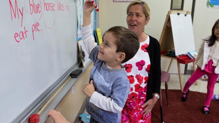 Adult and child writing on a whiteboard in a classroom