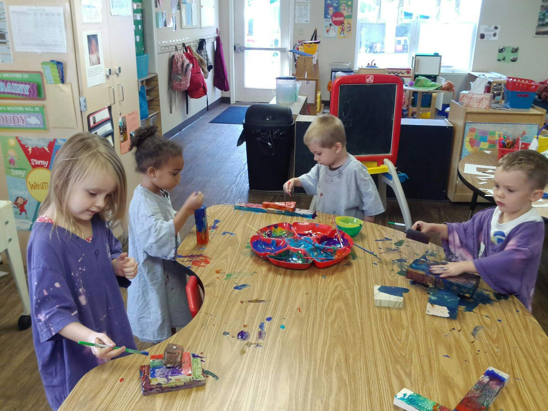 Four children painting at a table in a classroom
