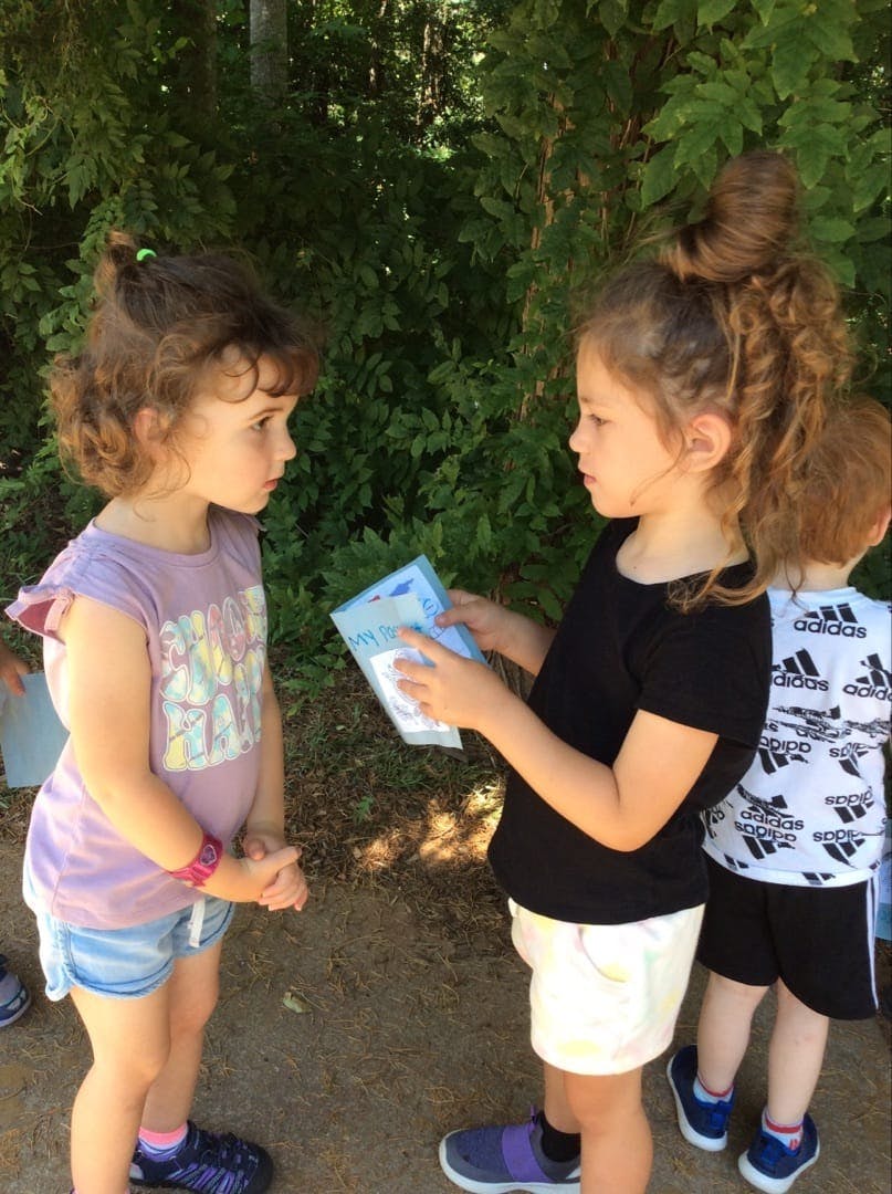 Child holding a small book and looking at another child