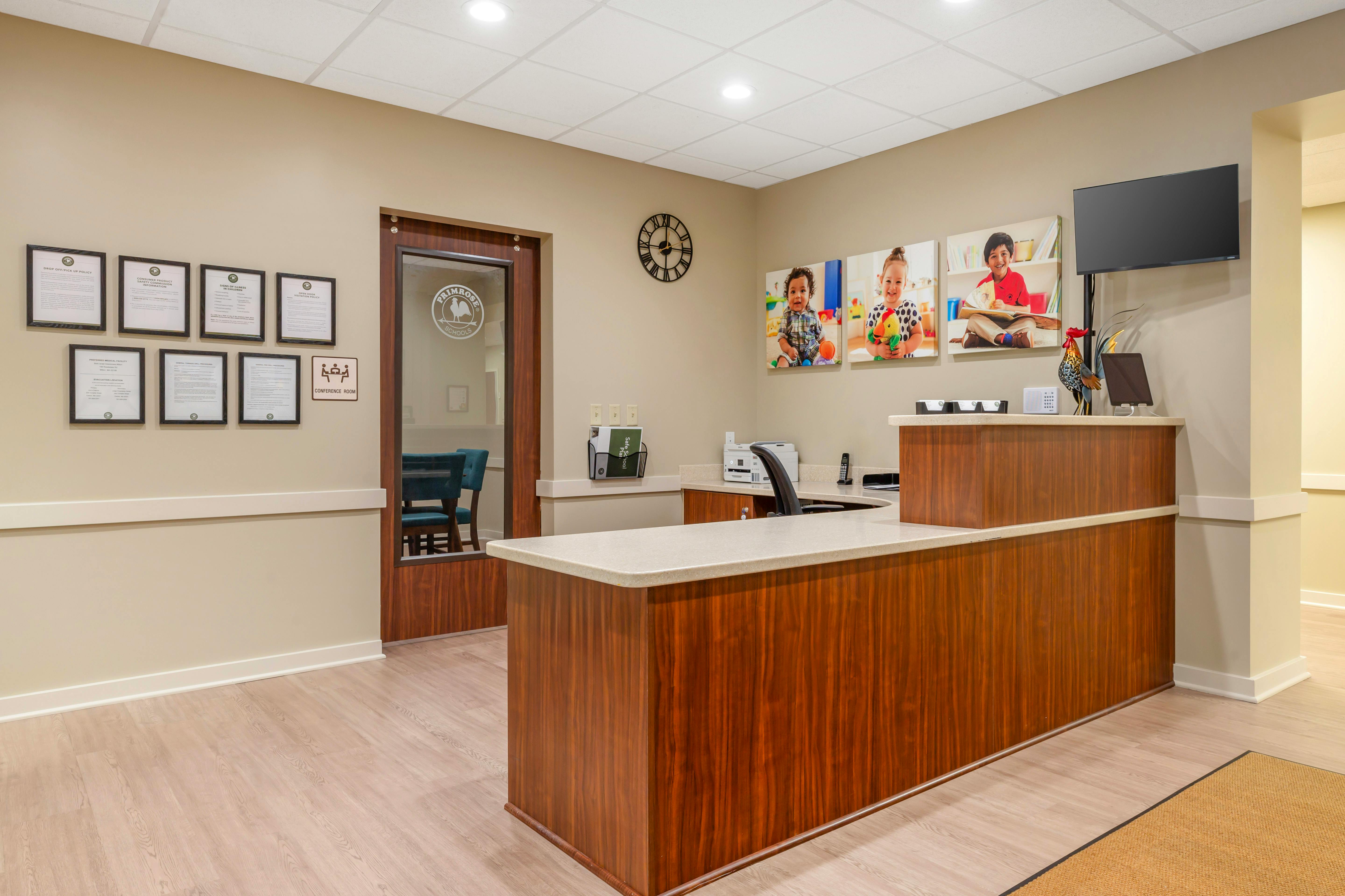 Reception desk with framed documents on wall, door to conference room, and photos