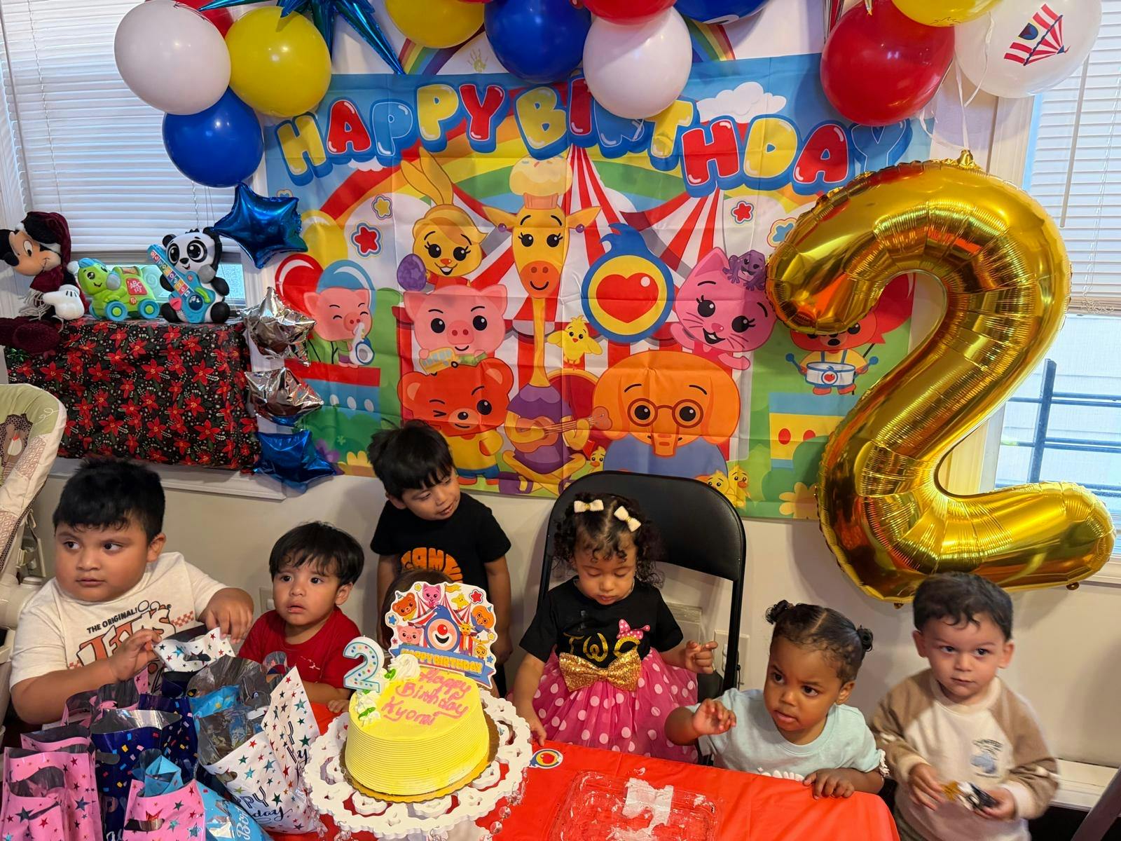 Group of children at a second birthday party with a cake and balloons