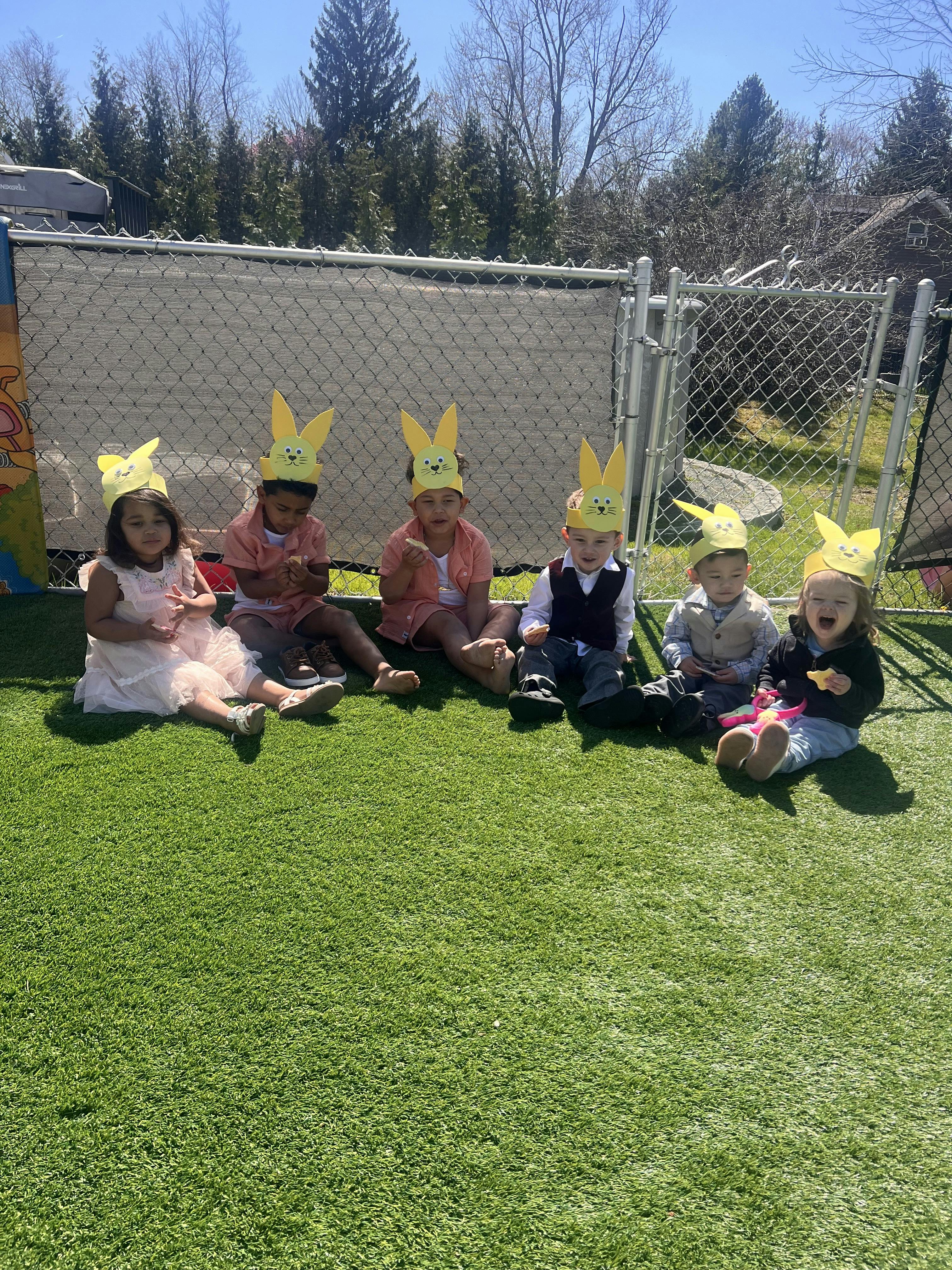 Five children wearing yellow bunny ear headbands sitting on grass