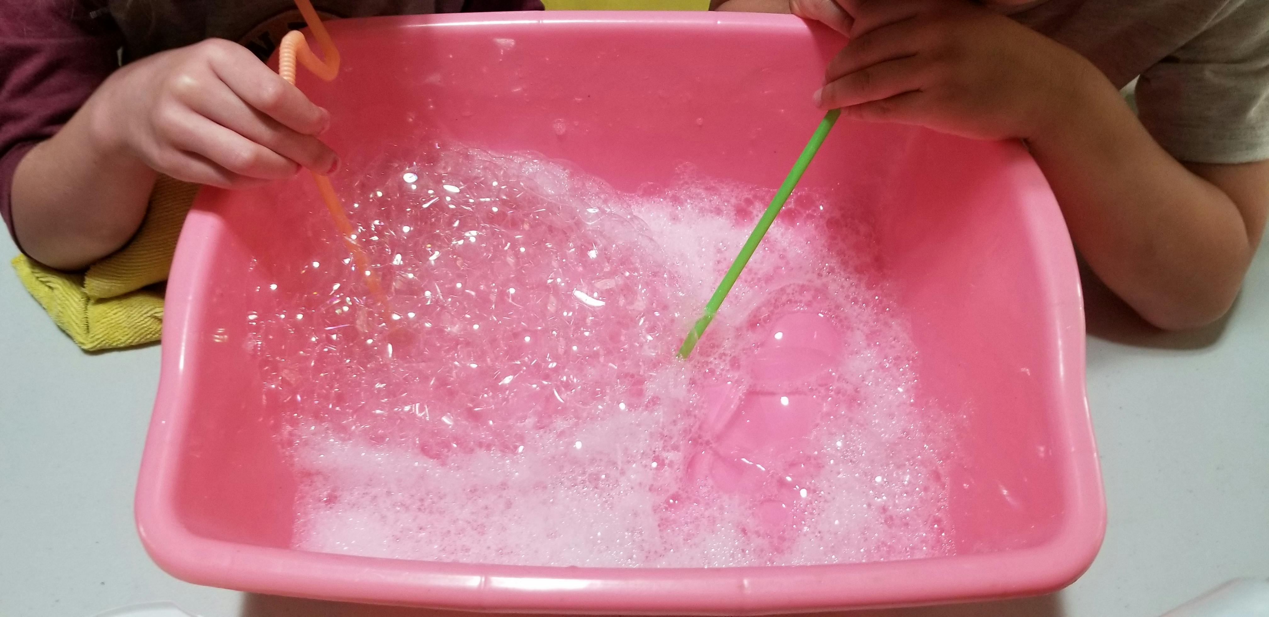 People using straws to blow bubbles in a pink basin