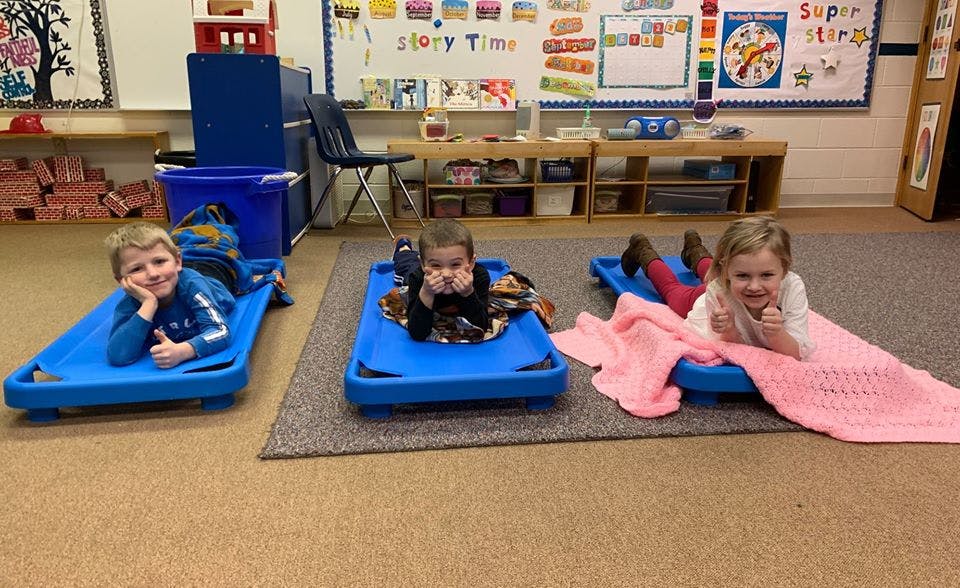 Three children lying on blue cots in a classroom
