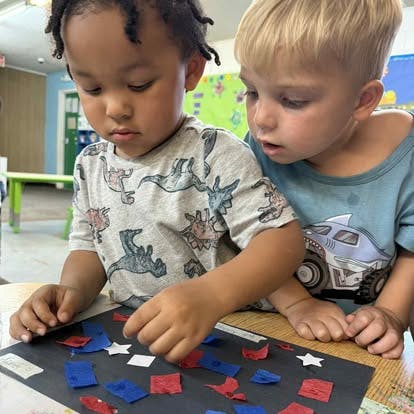 Two children doing a craft with red, white, and blue paper shapes