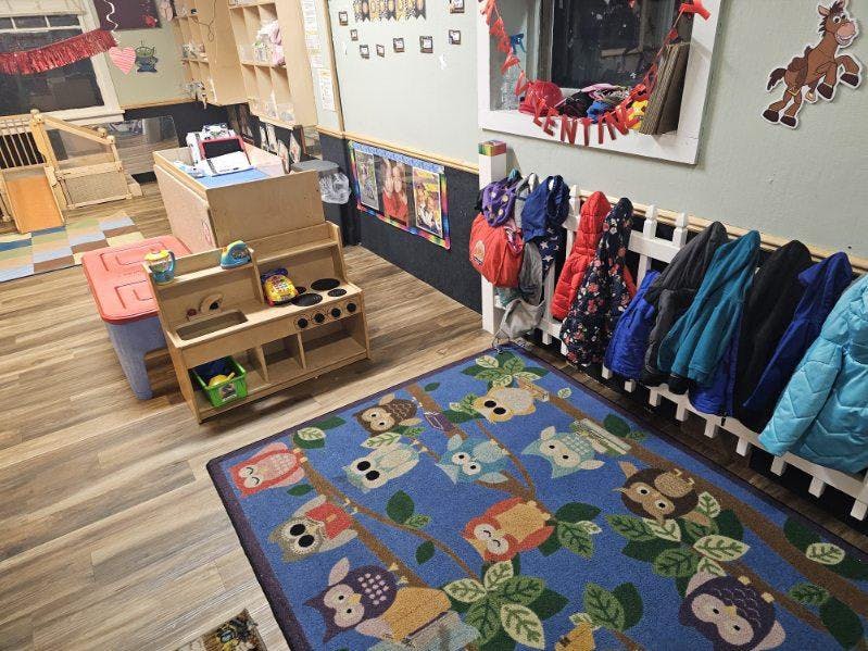 Playroom with toy kitchen, blue rug, and coats on a rack