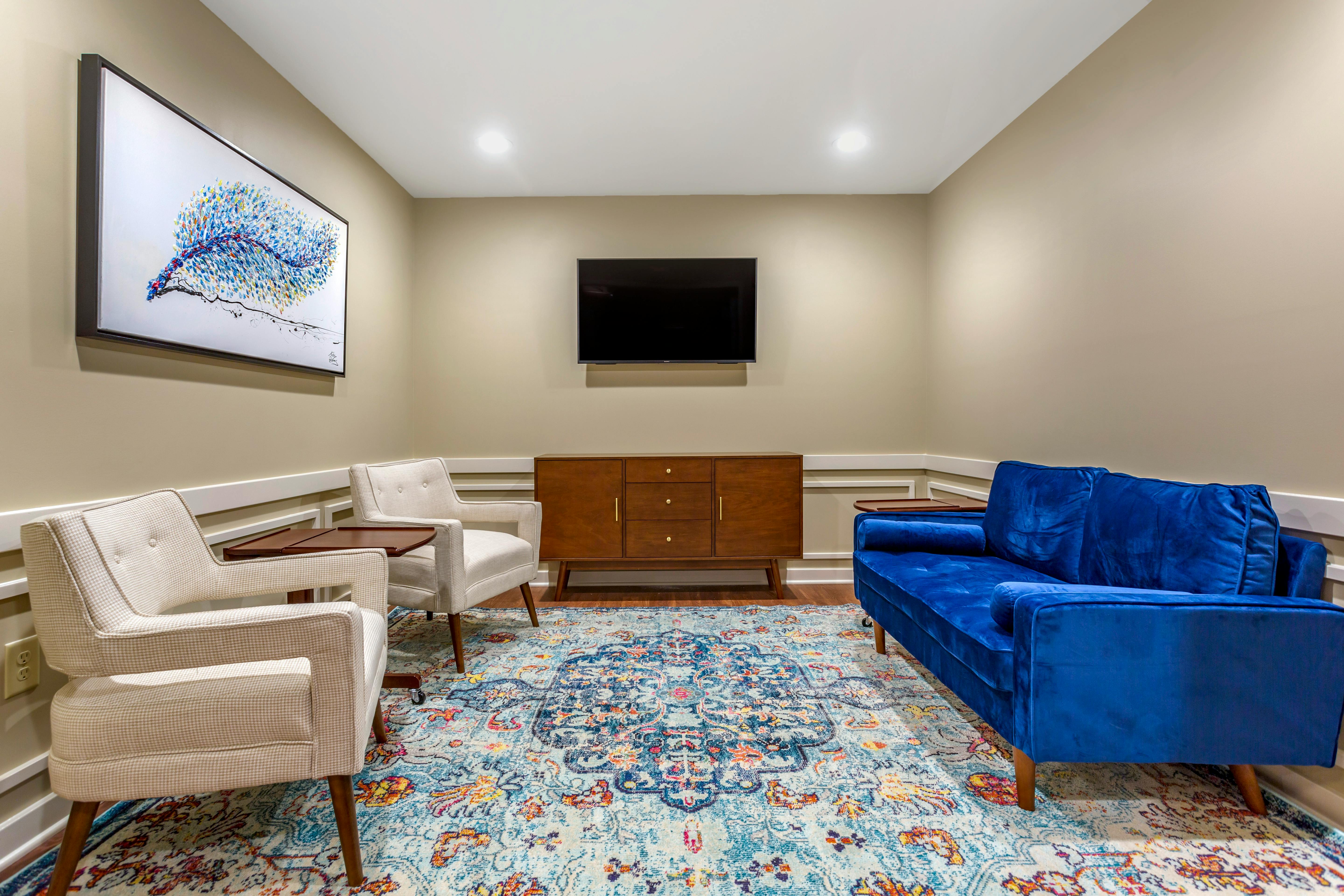 Living room with blue sofa, two chairs, abstract painting, TV, and patterned rug