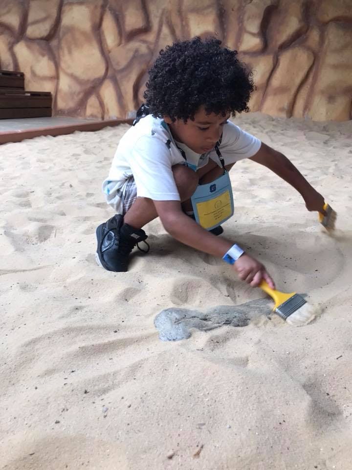 Child kneeling in sand, brushing sand away from an object