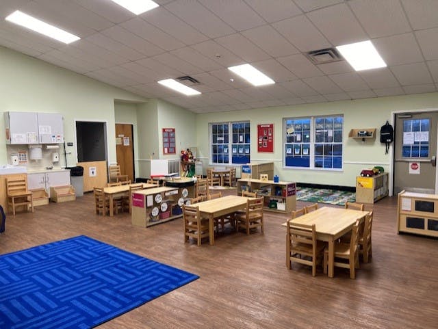 Empty classroom with small wooden tables and chairs, and a blue rug