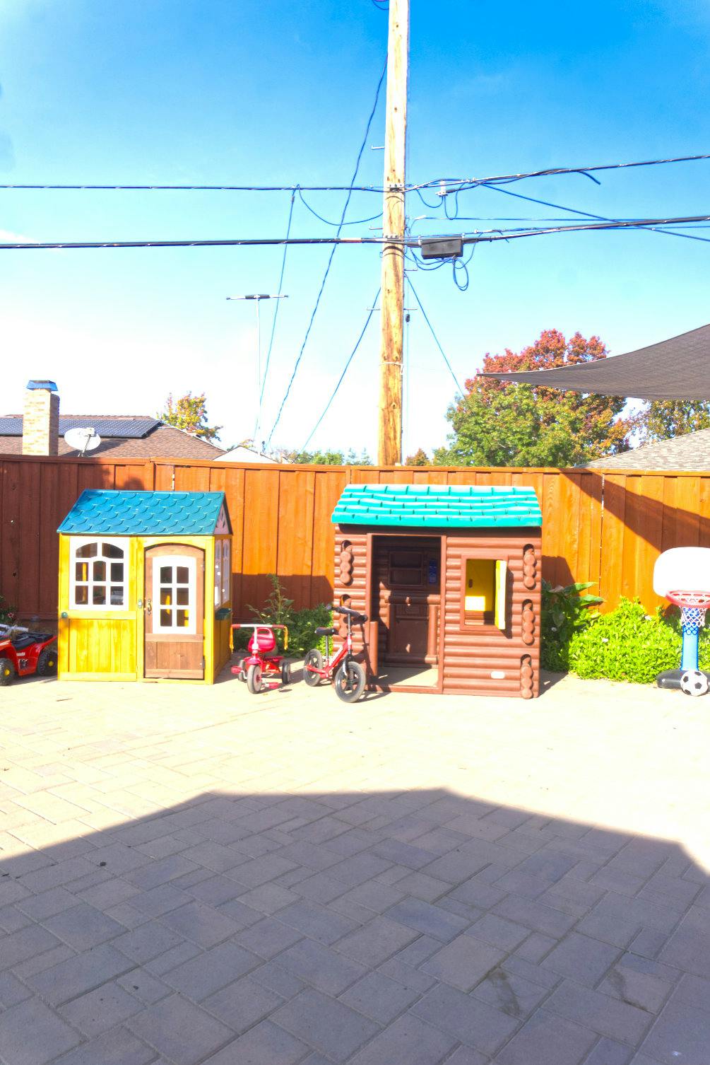 Two playhouses and children's bikes on a paved patio