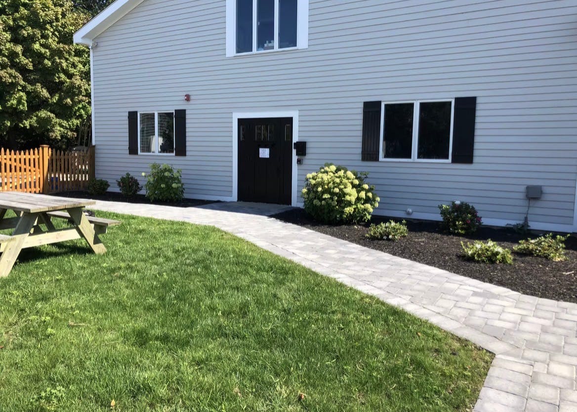 Building with light gray siding, dark door and shutters, green lawn, picnic table