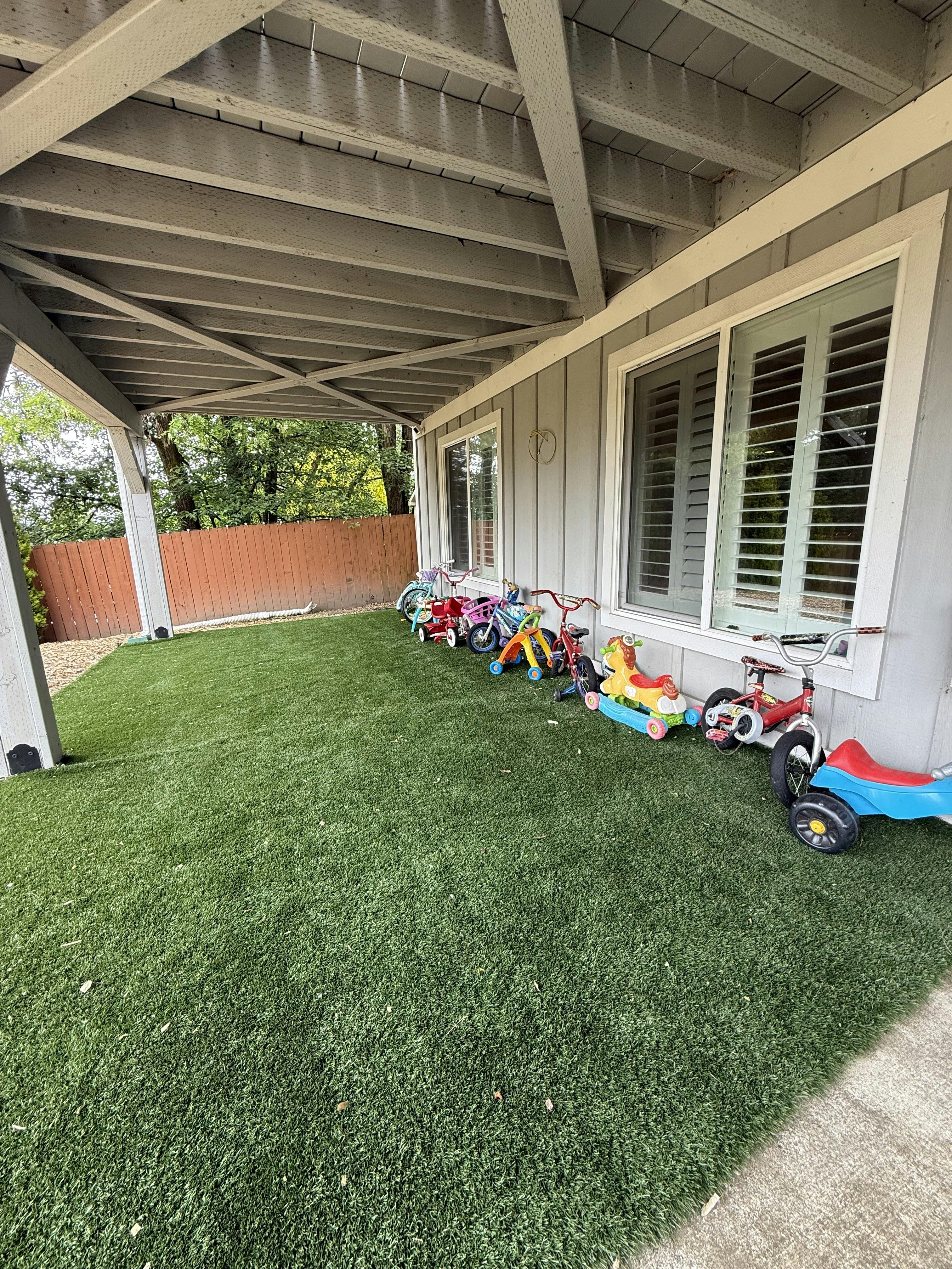 Row of children's ride-on toys and bicycles on a patio with artificial grass