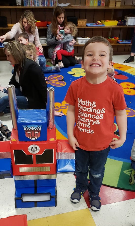 Child in red shirt standing next to a toy robot