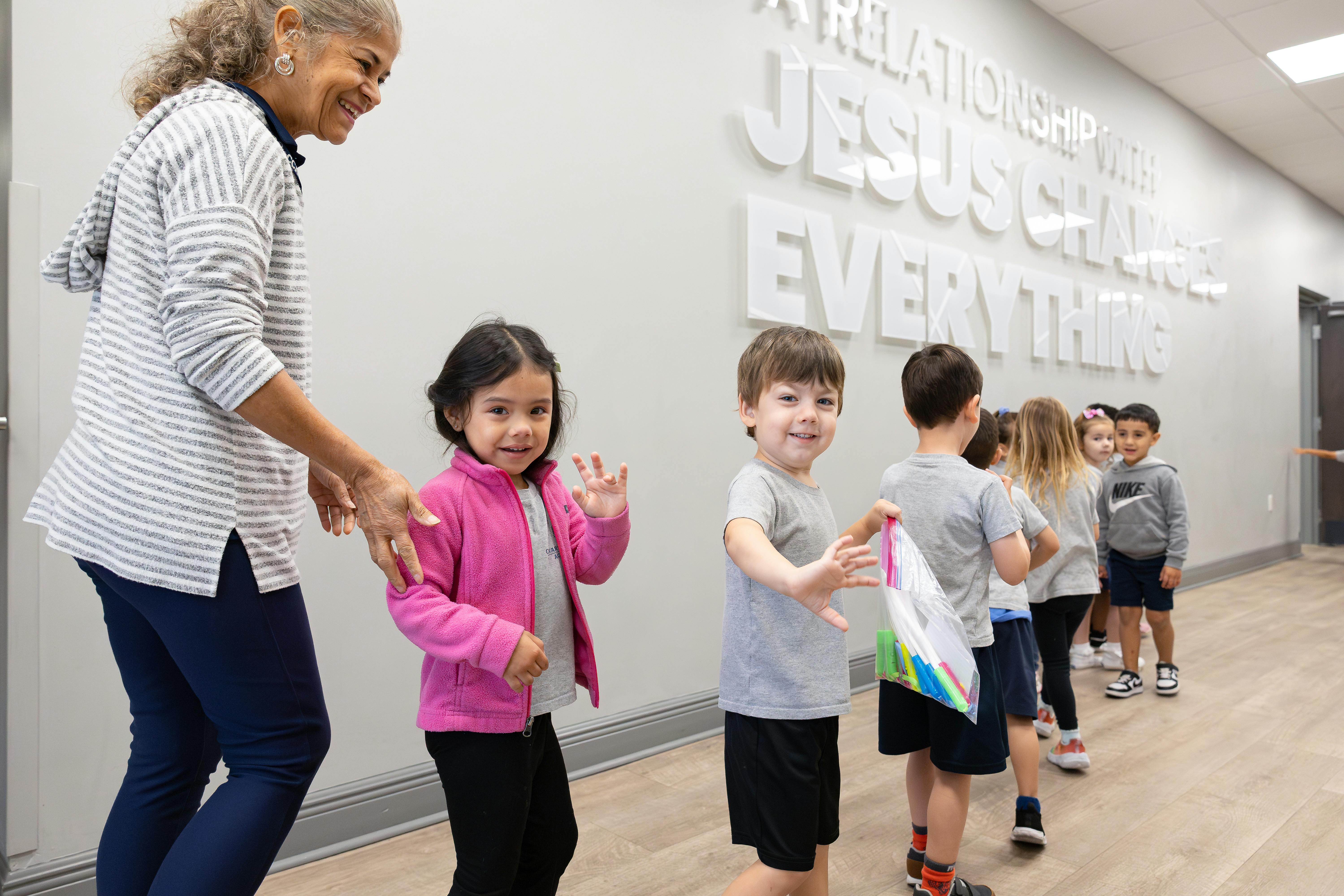 Adult person with children in a line, children are smiling and waving