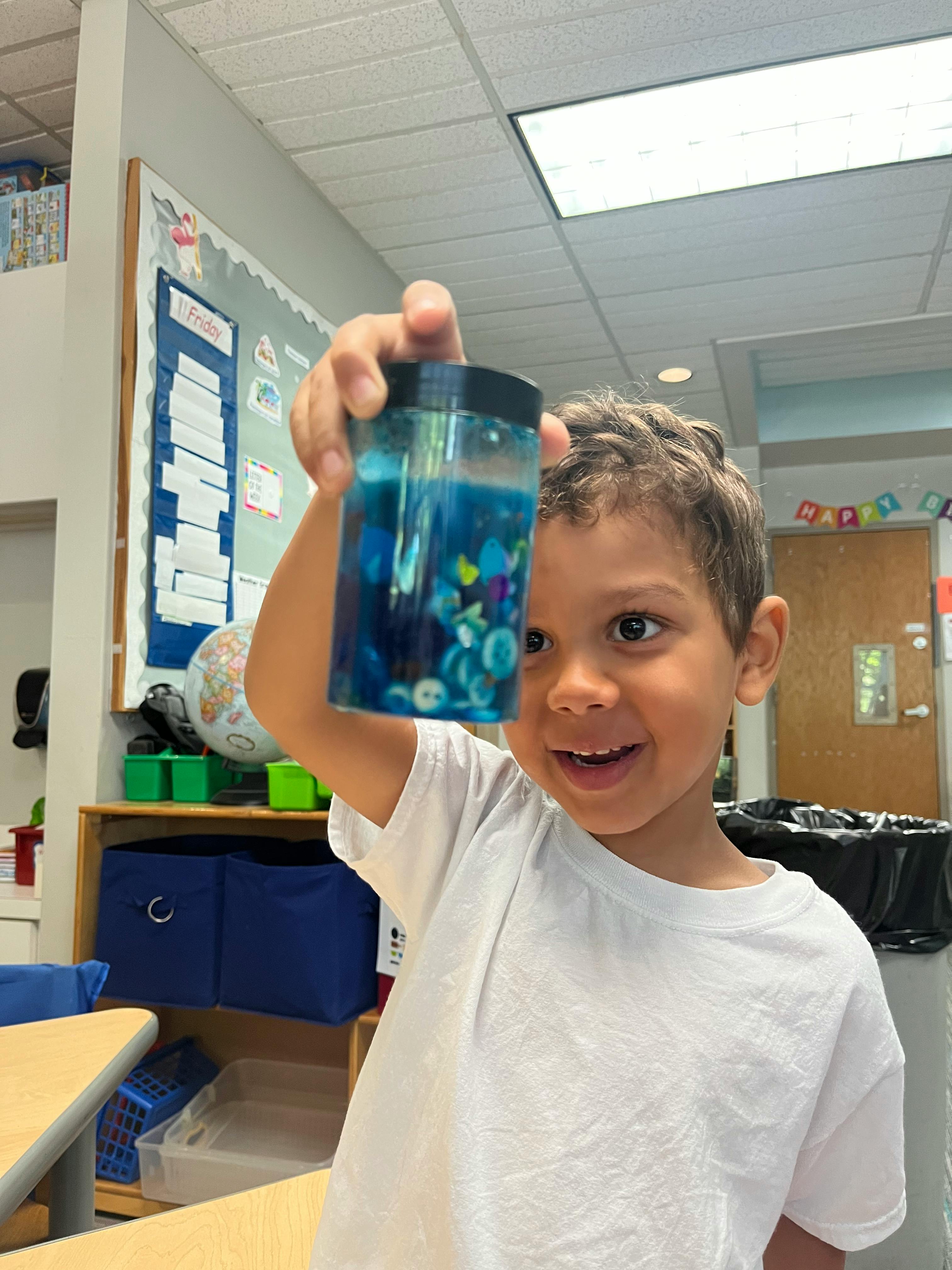 Child holding up a jar with blue liquid and small objects
