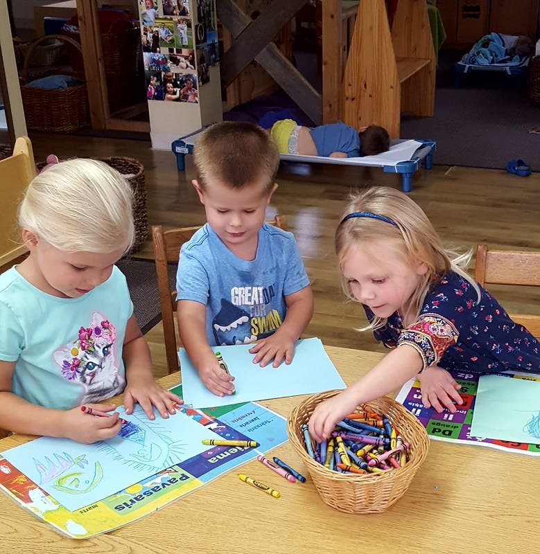 Three children coloring at a table in a classroom