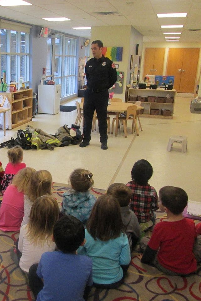 Adult in uniform standing in front of children sitting on floor in a classroom