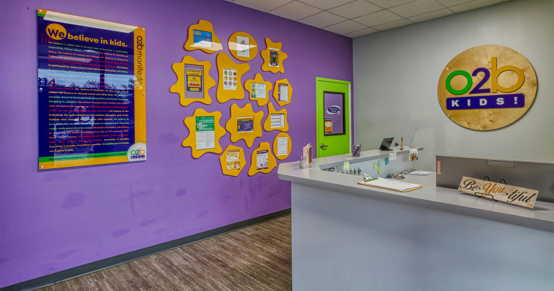 reception area with a purple wall, yellow framed notices, and a "Be You-tiful" sign
