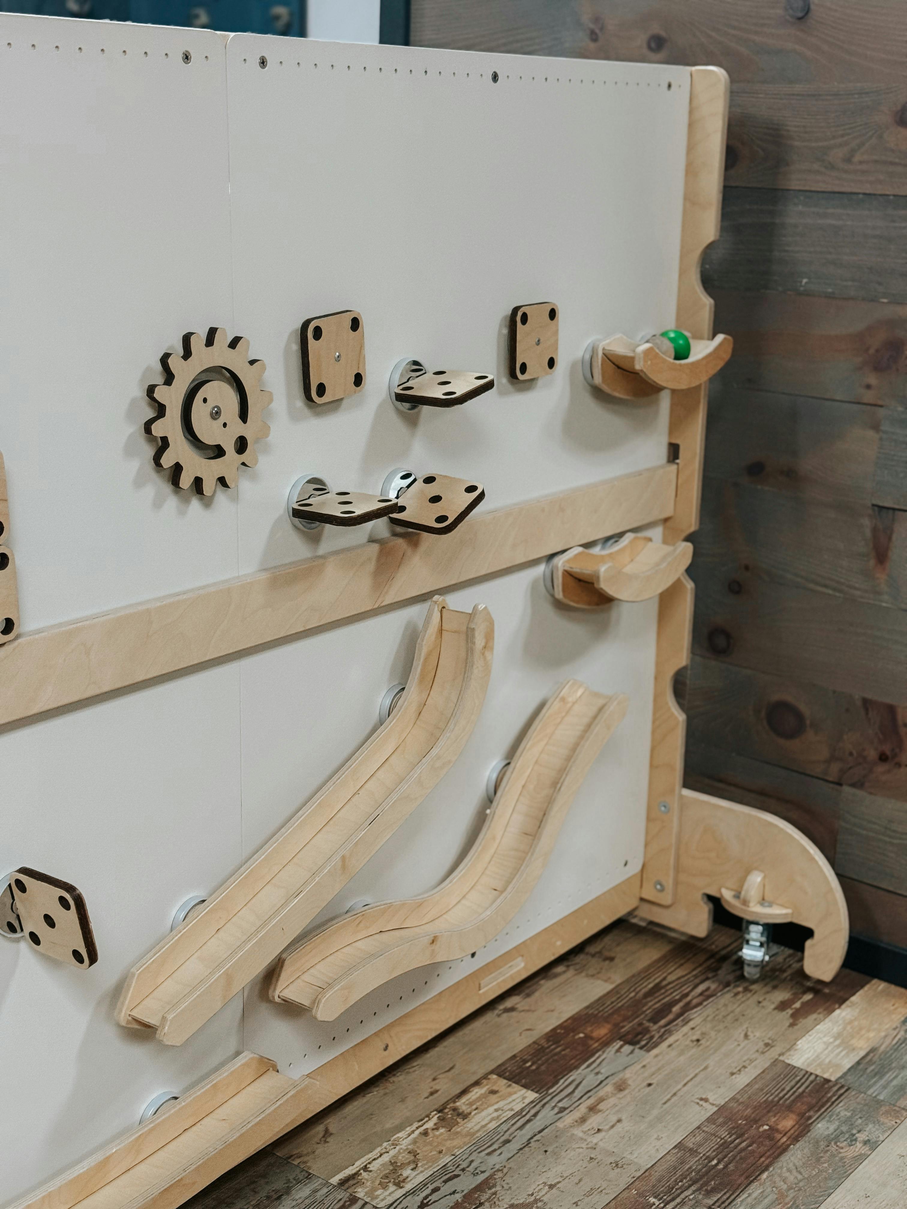 Wooden activity board with a gear, ramps, and a green ball