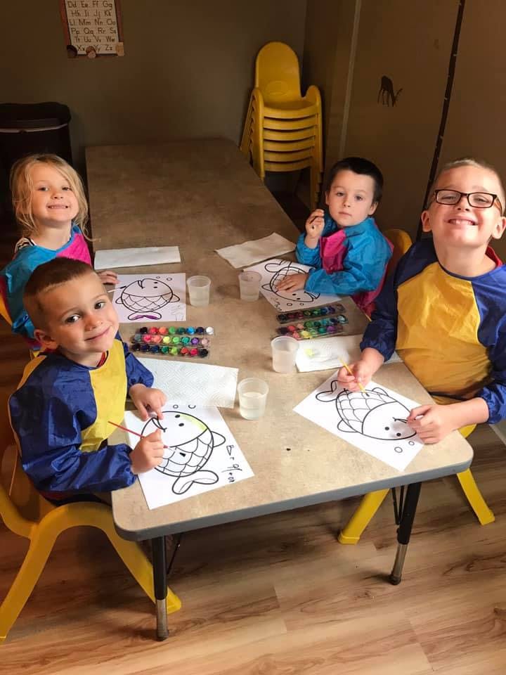 Four children painting fish pictures at a table