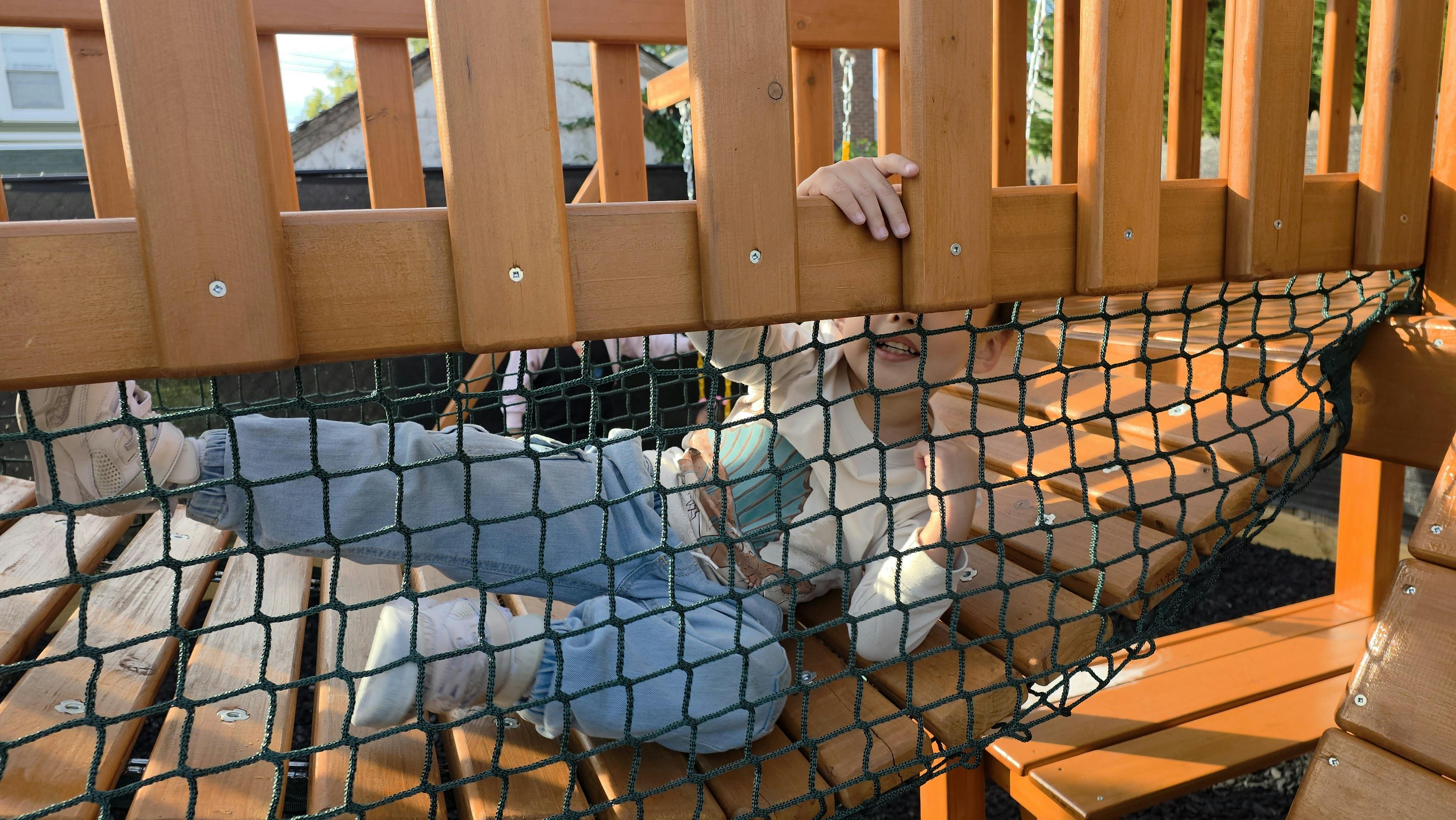 Child lying on a wooden playground structure behind safety netting