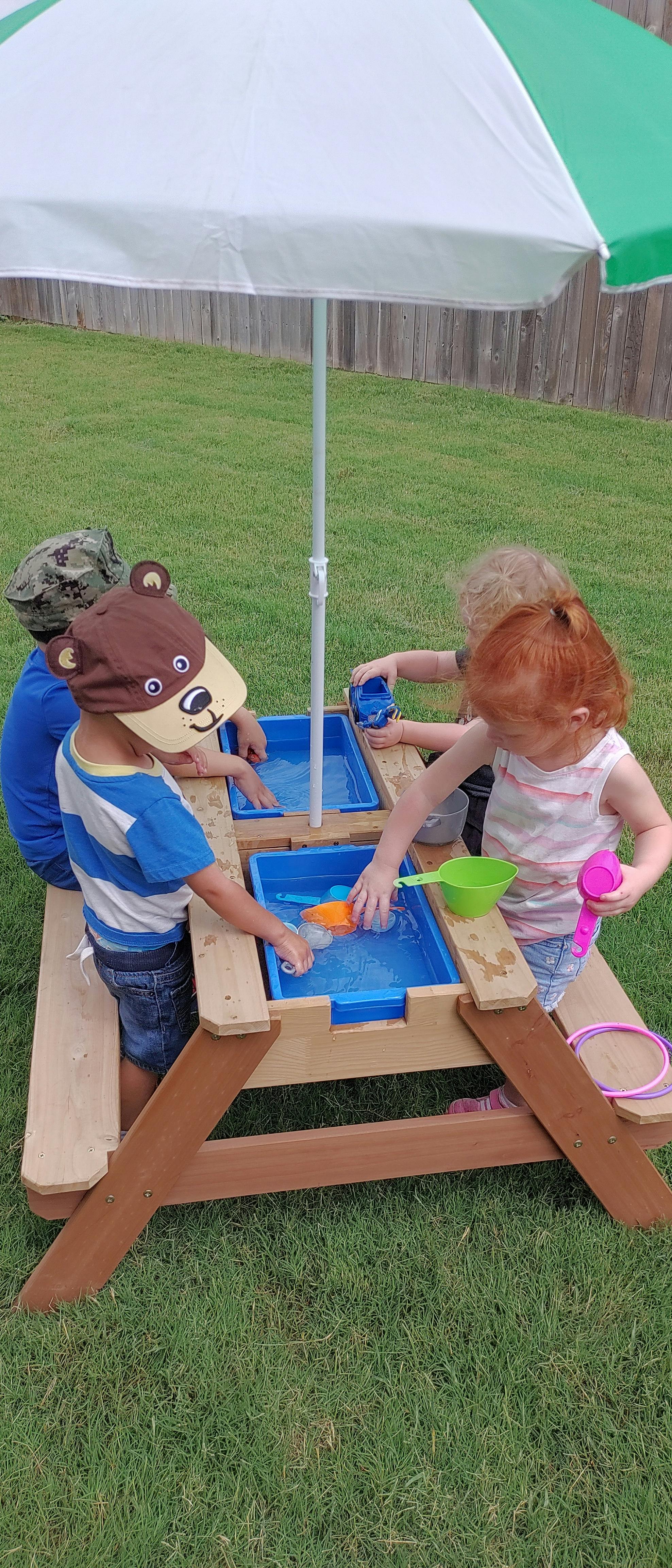 Children playing with water at a wooden activity table outdoors