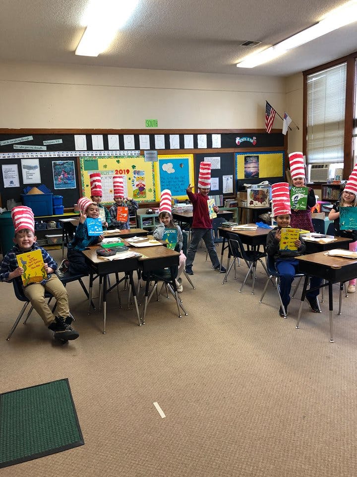 Children in a classroom wearing red and white striped hats and holding books