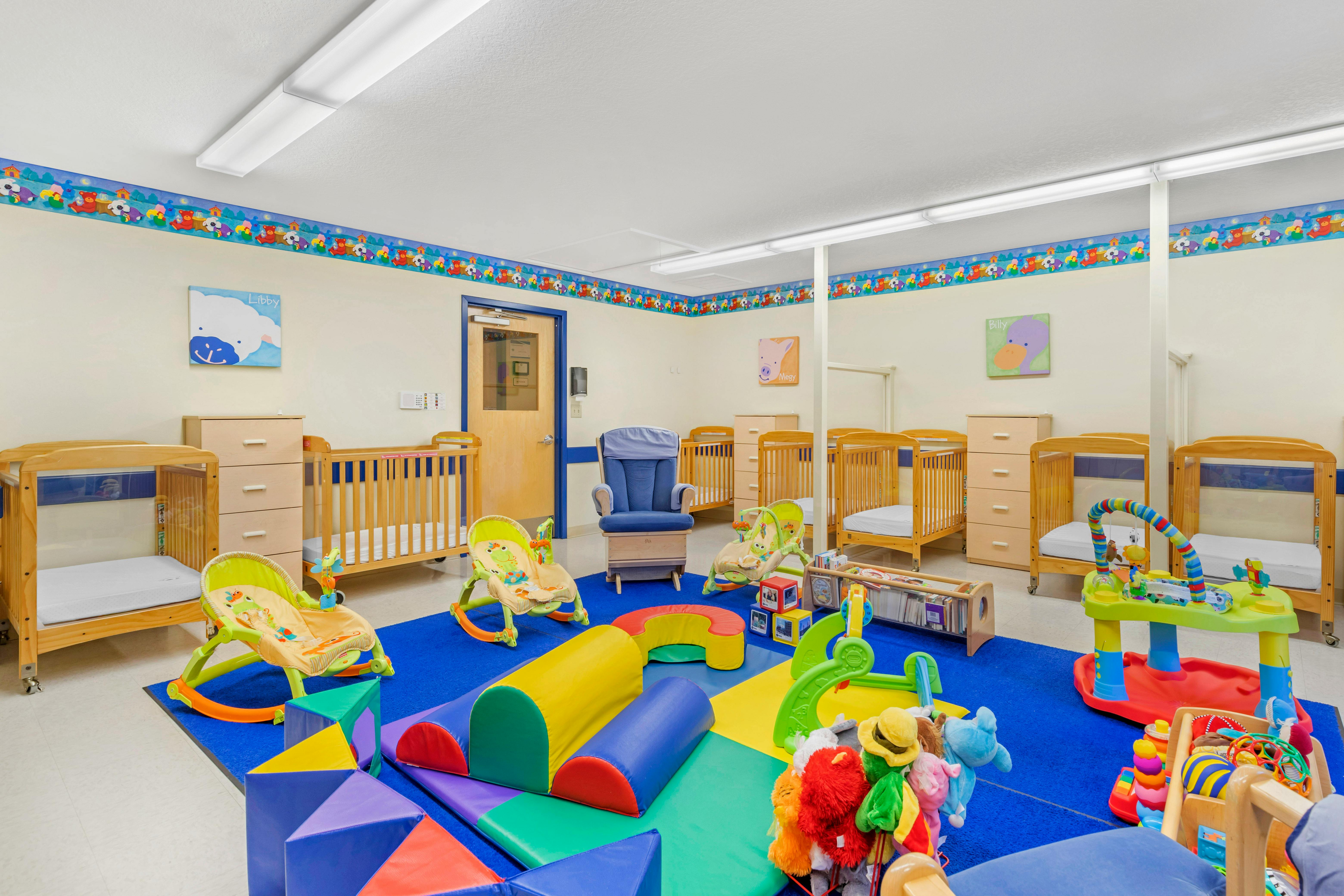 An empty nursery room with cribs, play mats, and a rocking chair