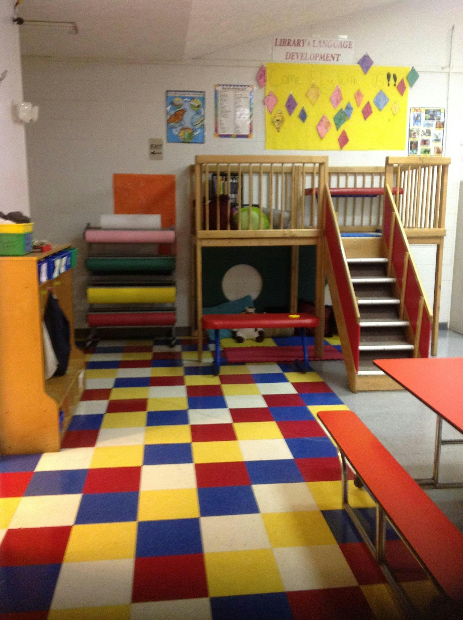 Indoor play area with a wooden structure, stairs, and colorful floor tiles