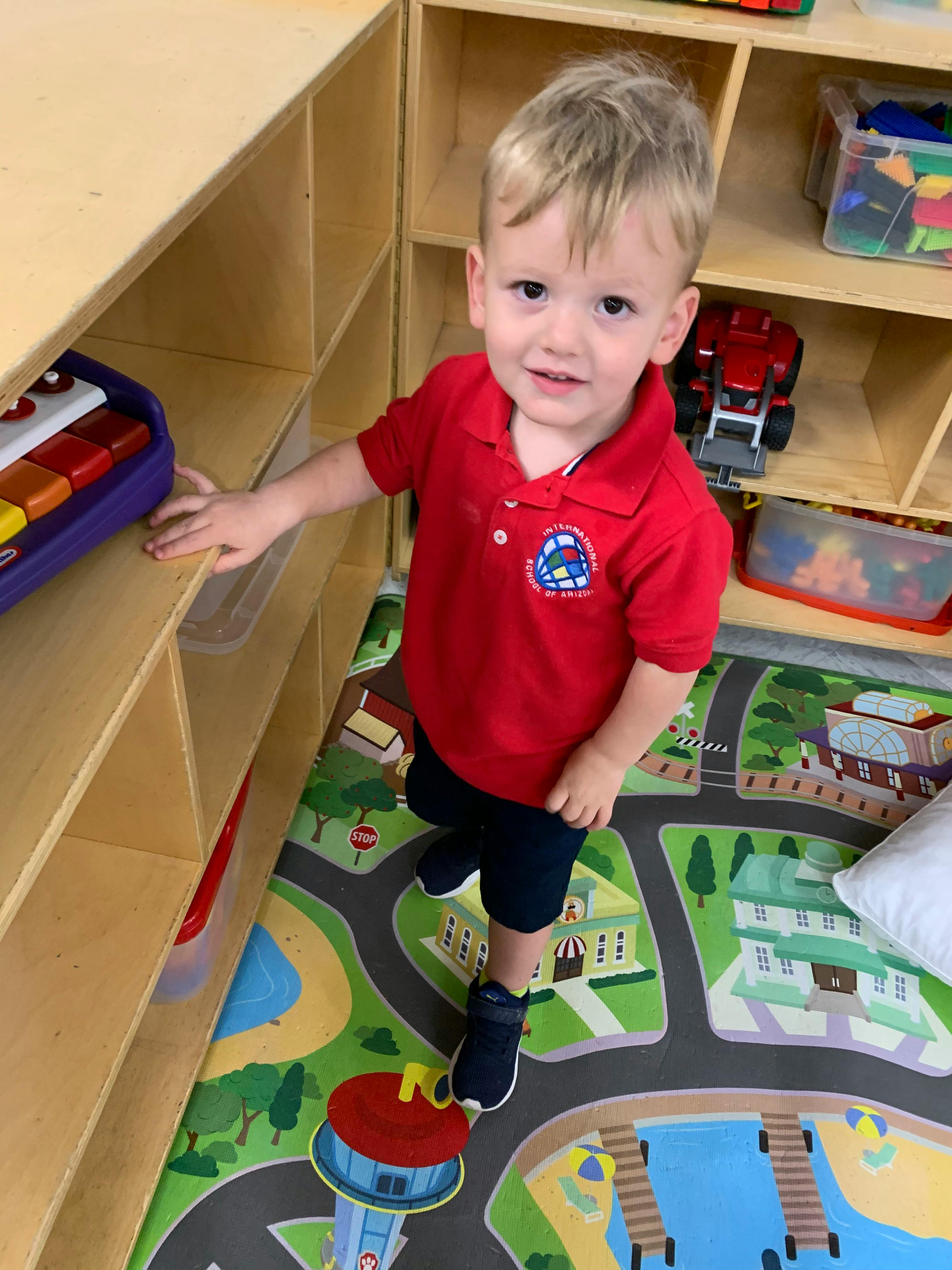 Child in a red shirt standing on a playmat in a classroom