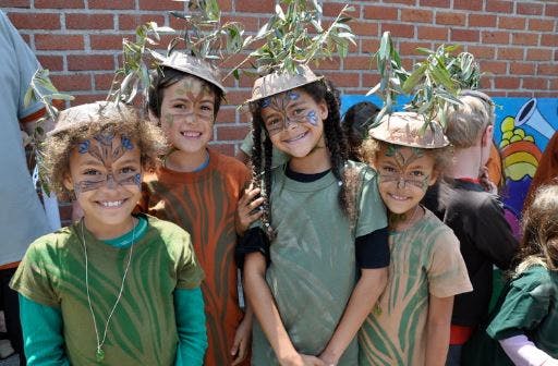 Four children in costumes with face paint and hats with leaves