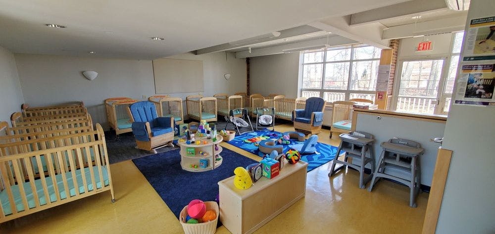 Room with multiple cribs, blue rug, and toys